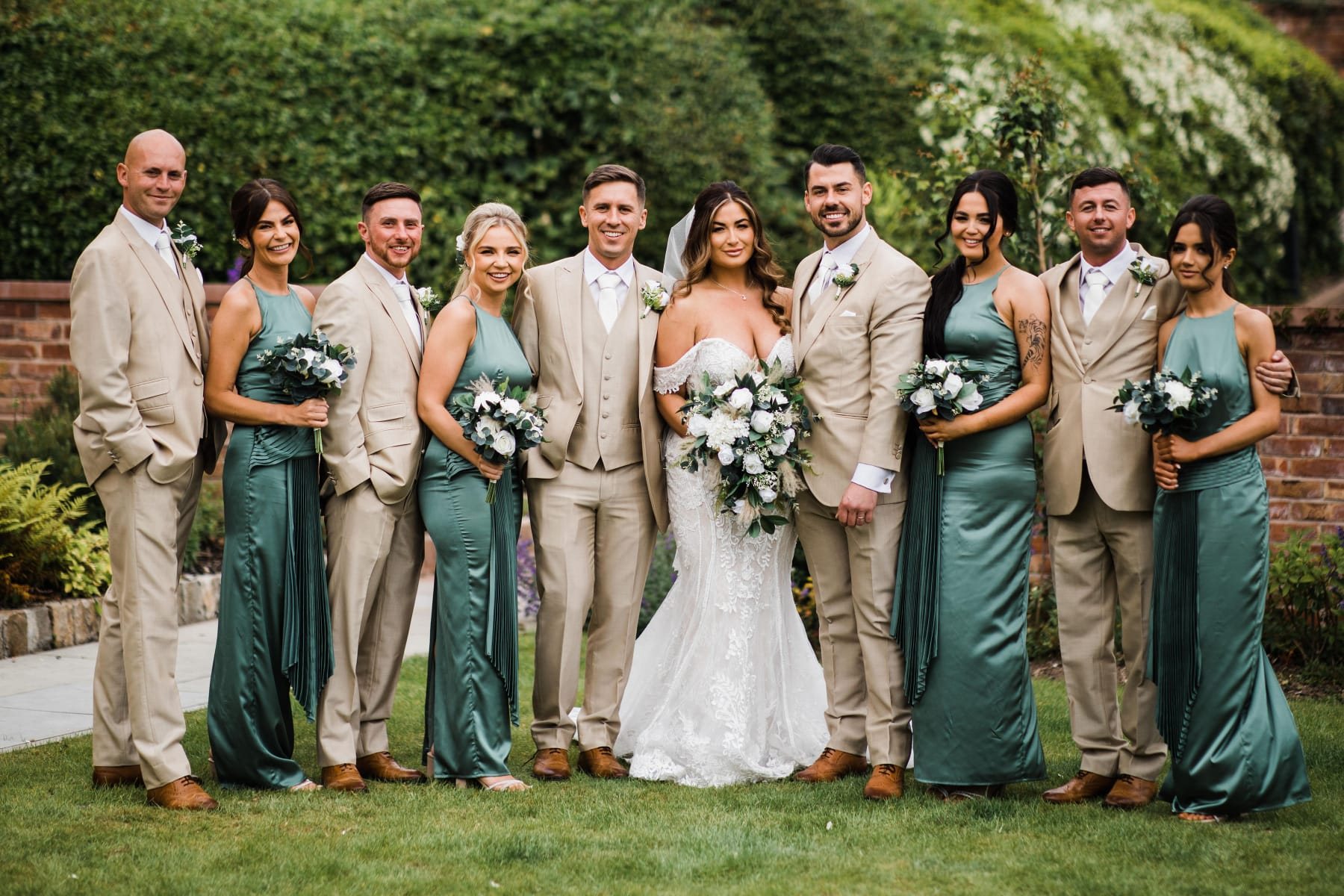 Wedding party in stone three-piece suits with bridesmaids in sage green